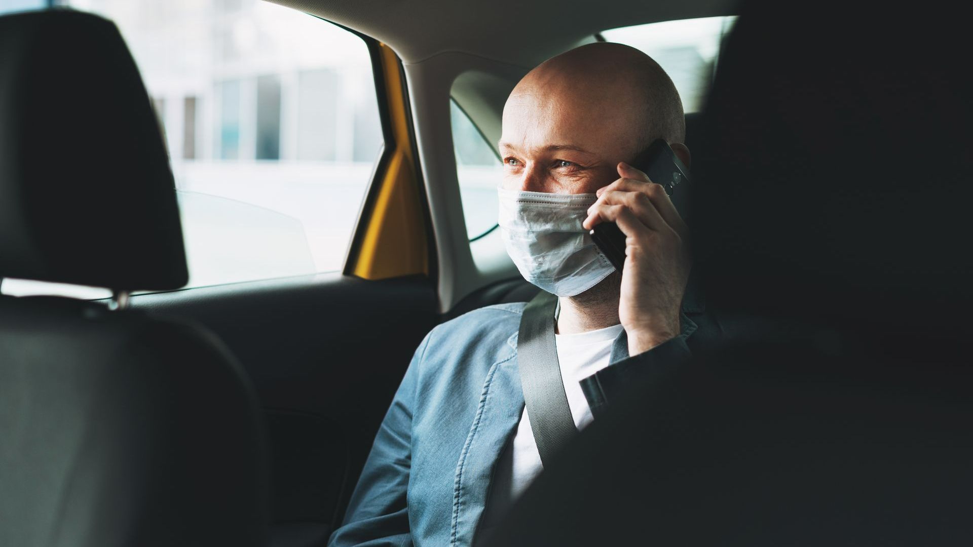Une personne portant un masque chirurgical au téléphone, assis dans un véhicule