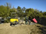 Une excavatrice jaune et une remorque-benne rose sur un chantier de terre, avec des arbres en arrière-plan
