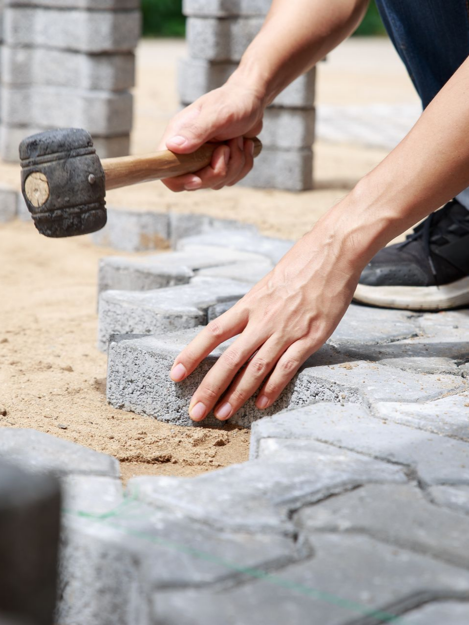 Des mains posent des pavés gris à l'aide d'un maillet en caoutchouc à l'extérieur