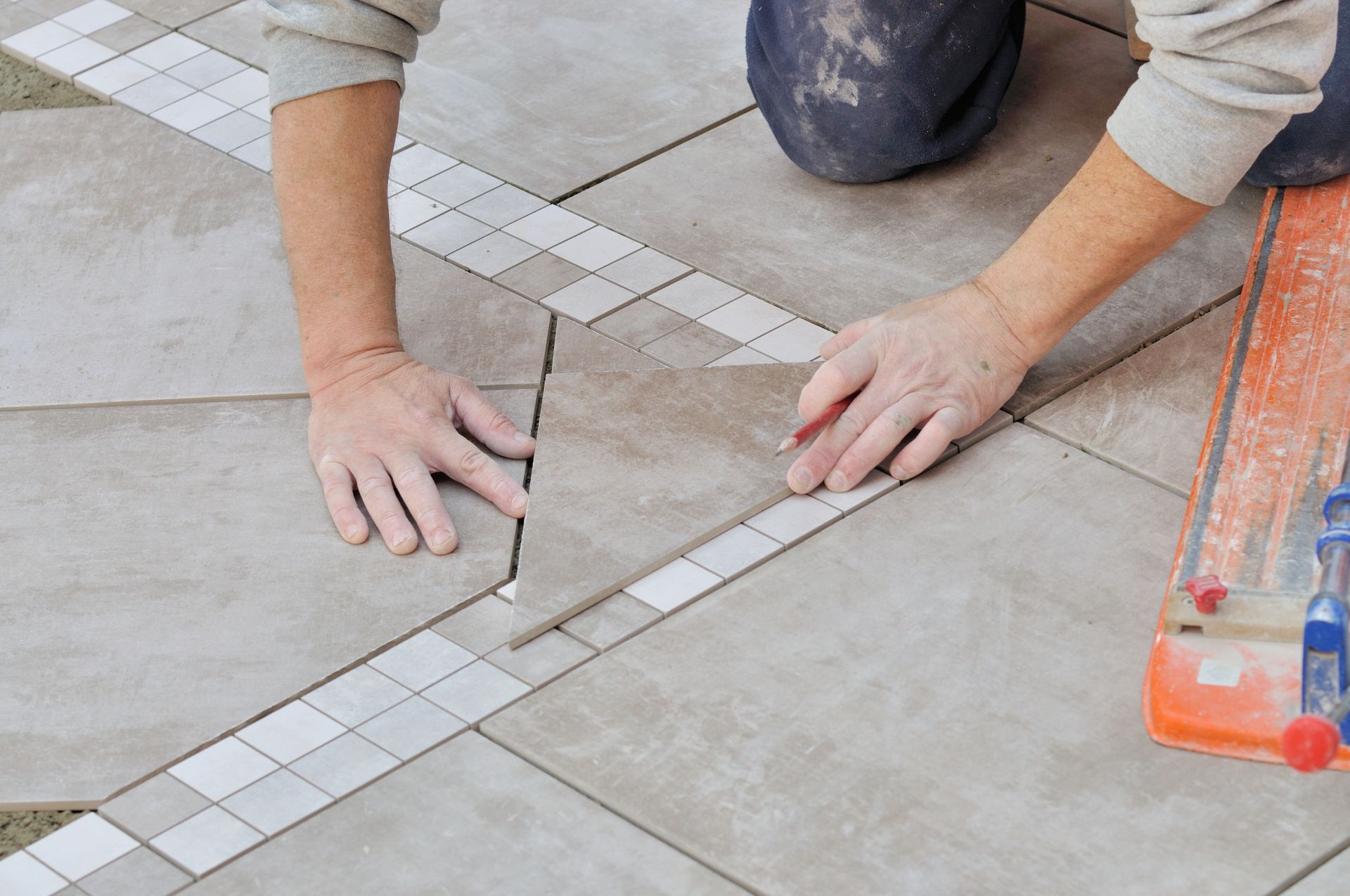 Un ouvrier aligne des carreaux de sol gris avec des bandes de mosaïque blanches lors de la pose