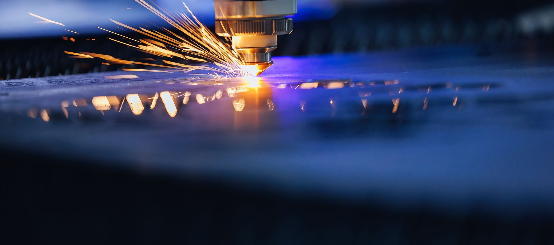 Laserleikkurin pää lähettää kirkkaita kipinöitä samalla kun se leikkaa tarkasti metallilevyä, jossa on sinisävyinen teollinen hehku.