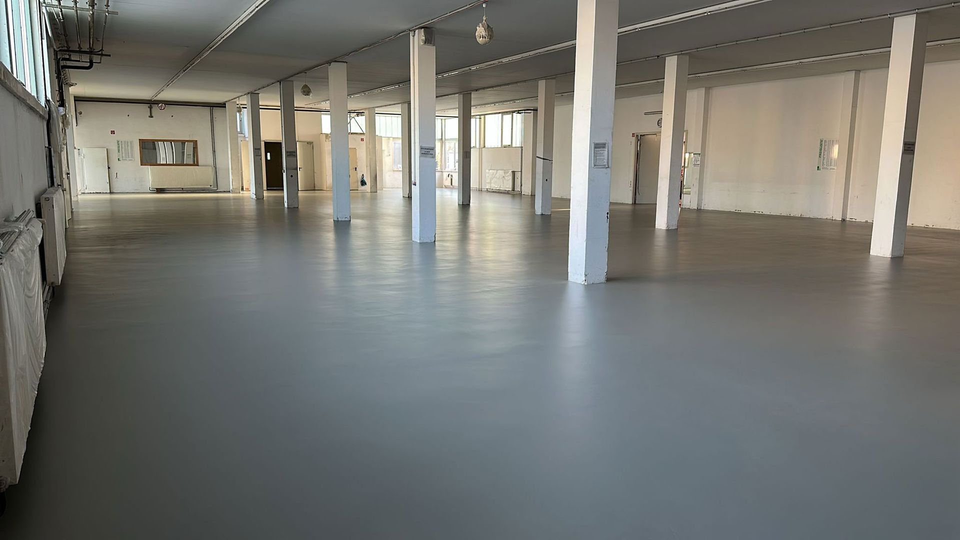 Leeres Lagerhausinterieur mit grauem Boden, weißen Säulen und Fenstern.