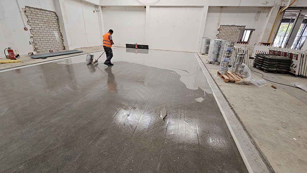 Ein Mann trägt in einer Baustelle Dichtmittel auf einen Betonboden auf.