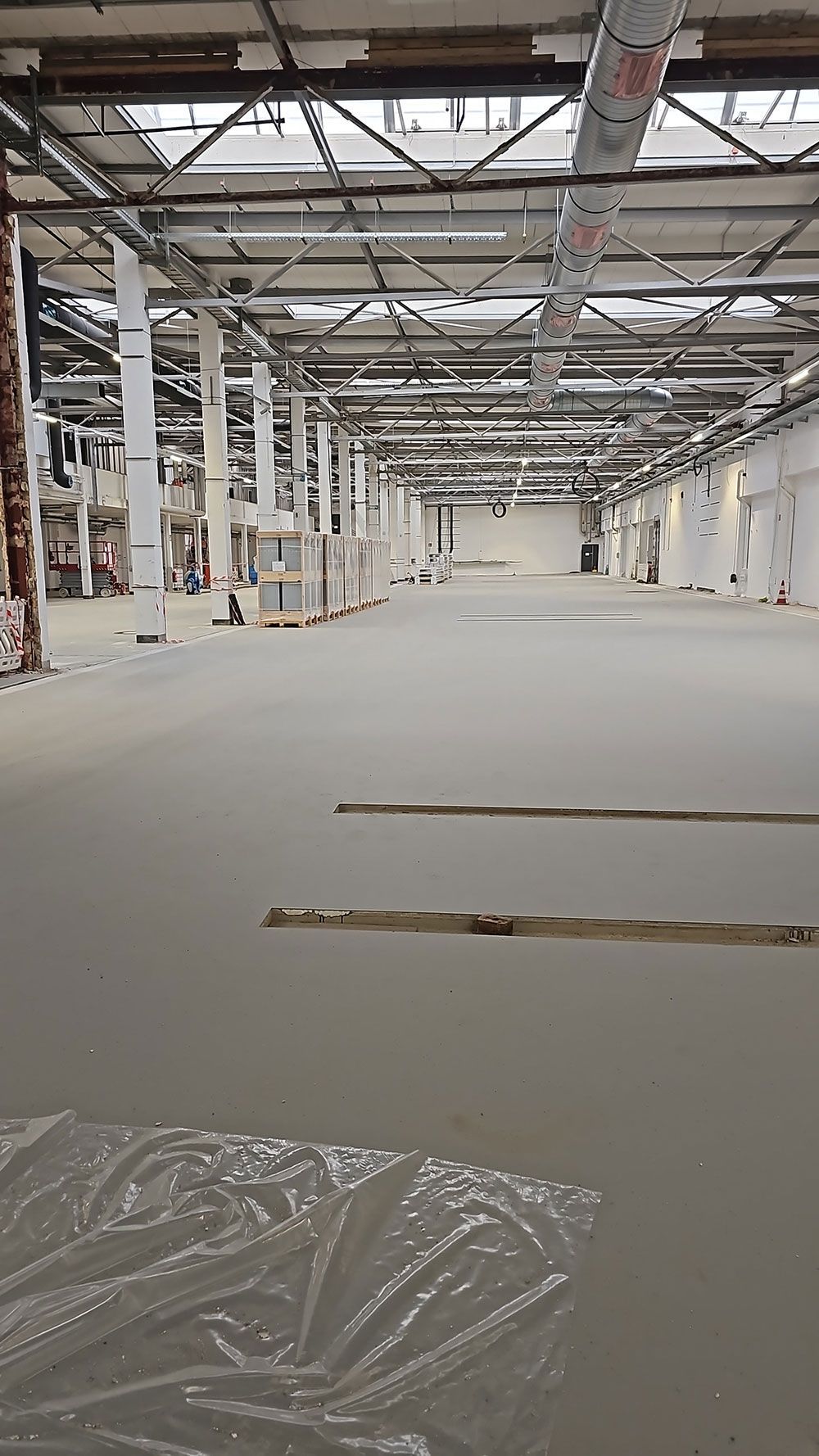 Innenansicht einer großen, leeren Industriehalle, die derzeit renoviert wird und über einen neuen Betonboden.