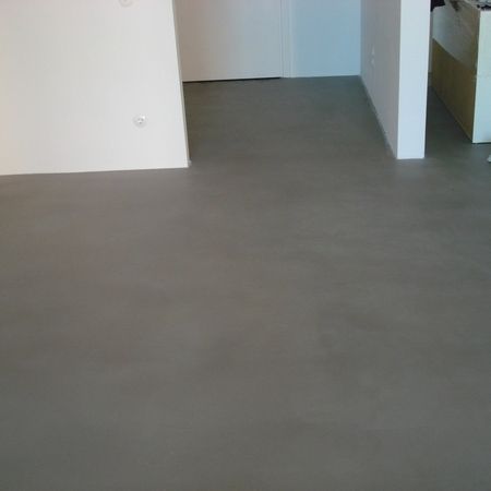 Grauer Betonboden in einem Raum mit weißen Wänden, der frisch verlegt und glatt aussieht.