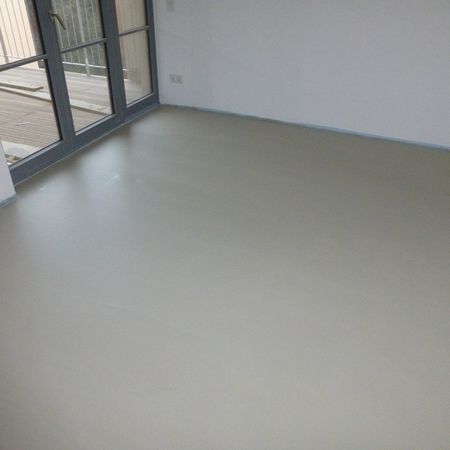 Leerer Raum mit hellgrauem Boden und weißen Wänden, links eine Glasschiebetür.