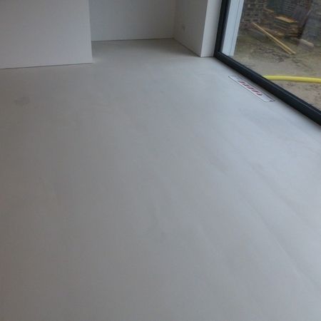 Hellgrauer Betonboden in einem Zimmer, durch den ein Fensterrahmen sichtbar ist.