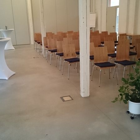 Reihen von Holzstühlen, die in einem großen Raum für eine Veranstaltung aufgestellt sind, in der Nähe von weißen Säulen.