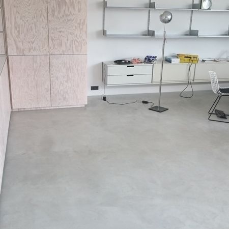 Hellgrauer Betonboden in einem Raum mit hellen Holzschränken, Regalen und einer Metalllampe.