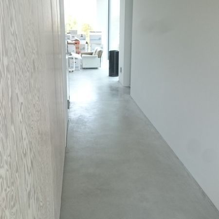 Flur mit hellgrauem Betonboden und weißen Wänden; Blick in einen anderen Raum.