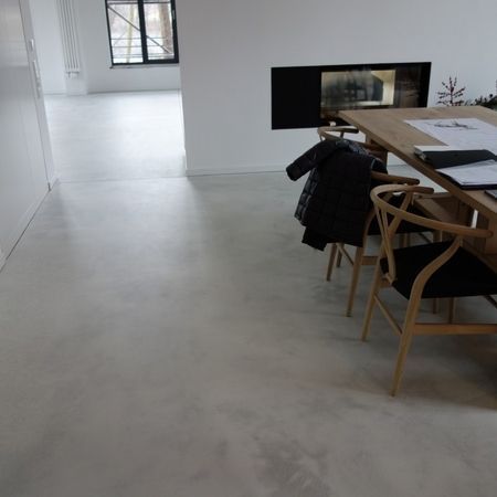 Hellgrauer Betonboden in einem modernen Interieur mit Esstisch, Stühlen und Kamin.
