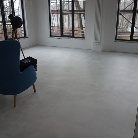 Blauer Sessel in einem weißen Zimmer mit großen Fenstern, einer schwarzen Stehlampe und weißen Wänden.