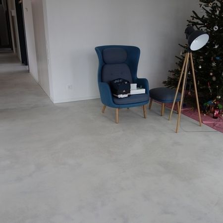 Blauer Sessel mit Fußhocker, Lampe und Weihnachtsbaum in einem Zimmer mit hellgrauem Boden.