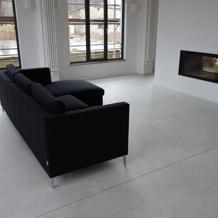 Schwarzes Sofa in einem modernen weißen Wohnzimmer mit Kamin und großen Fenstern.