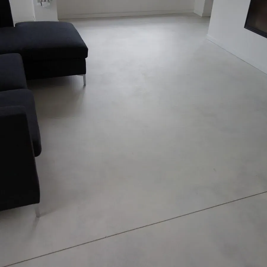 Schwarzes Ecksofa auf hellgrauem, poliertem Betonboden in einem modernen Wohnzimmer.