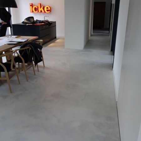 Hellgrauer Betonboden in einem offenen Raum mit Essbereich und Flur, der in einen dunklen Raum führt.