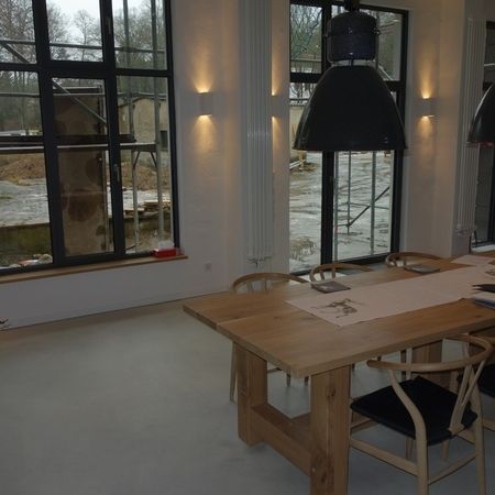 Esszimmer mit großen Fenstern, Holztisch und -stühlen sowie Beleuchtung im Industriestil.