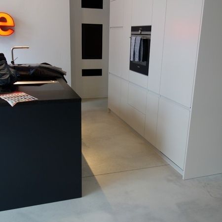 Moderne Küche mit schwarzer Kochinsel, weißen Schränken und Betonboden.