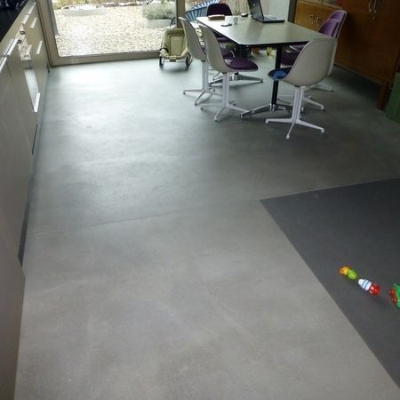 Innenraum mit grauem Betonboden, Tisch mit Stühlen, Fenster, Spielzeug.