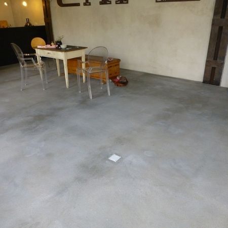 Ein Zimmer mit poliertem Betonboden, einem Tisch, Stühlen und einer kleinen Truhe.