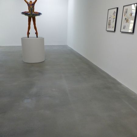 Eine moderne Kunstgalerie mit einer Ballerina-Statue auf einem Sockel; gerahmte Zeichnungen an der Wand.