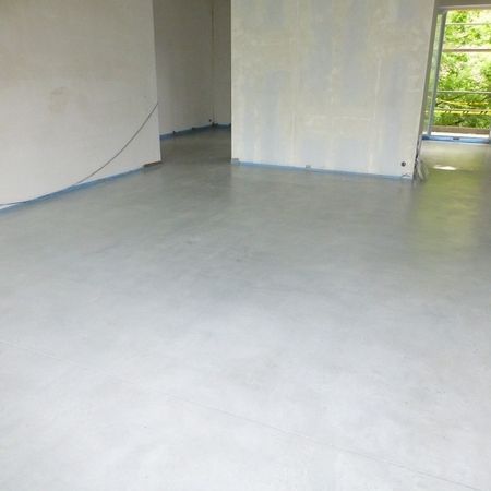 Hellgrauer Betonboden in einem unfertigen Raum mit weißen Wänden und einem Fenster.