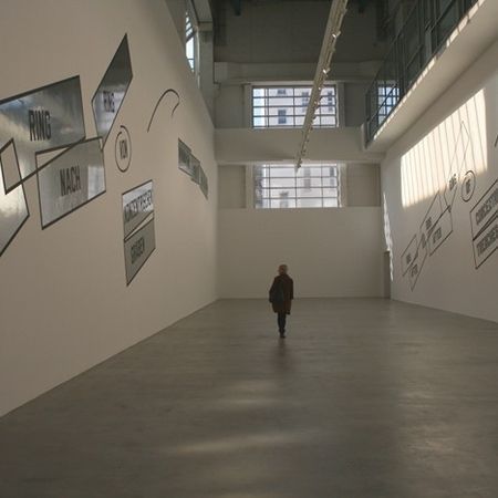 Eine Frau geht durch eine Galerie für moderne Kunst. Weiße Wände mit Texttafeln.