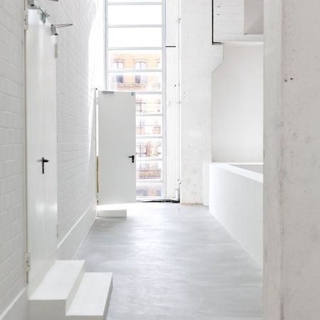 Weißer Flur mit Türen, Fenster und Betonboden.