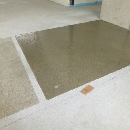 Grauer Betonboden mit helleren Abschnitten und einem Etikett.