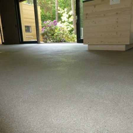 Innenraum mit hellgrauem Betonboden und offenen Türen zu einem mit Laubwerk bewachsenen Hof.