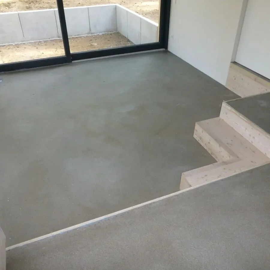 Grauer Betonboden mit hellen Holztreppen, die zu einer Glastür hinunterführen.