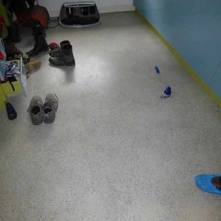 Grauer Boden mit verstreuten Schuhen an einer blauen Wand. Einige Gegenstände in der Ecke.