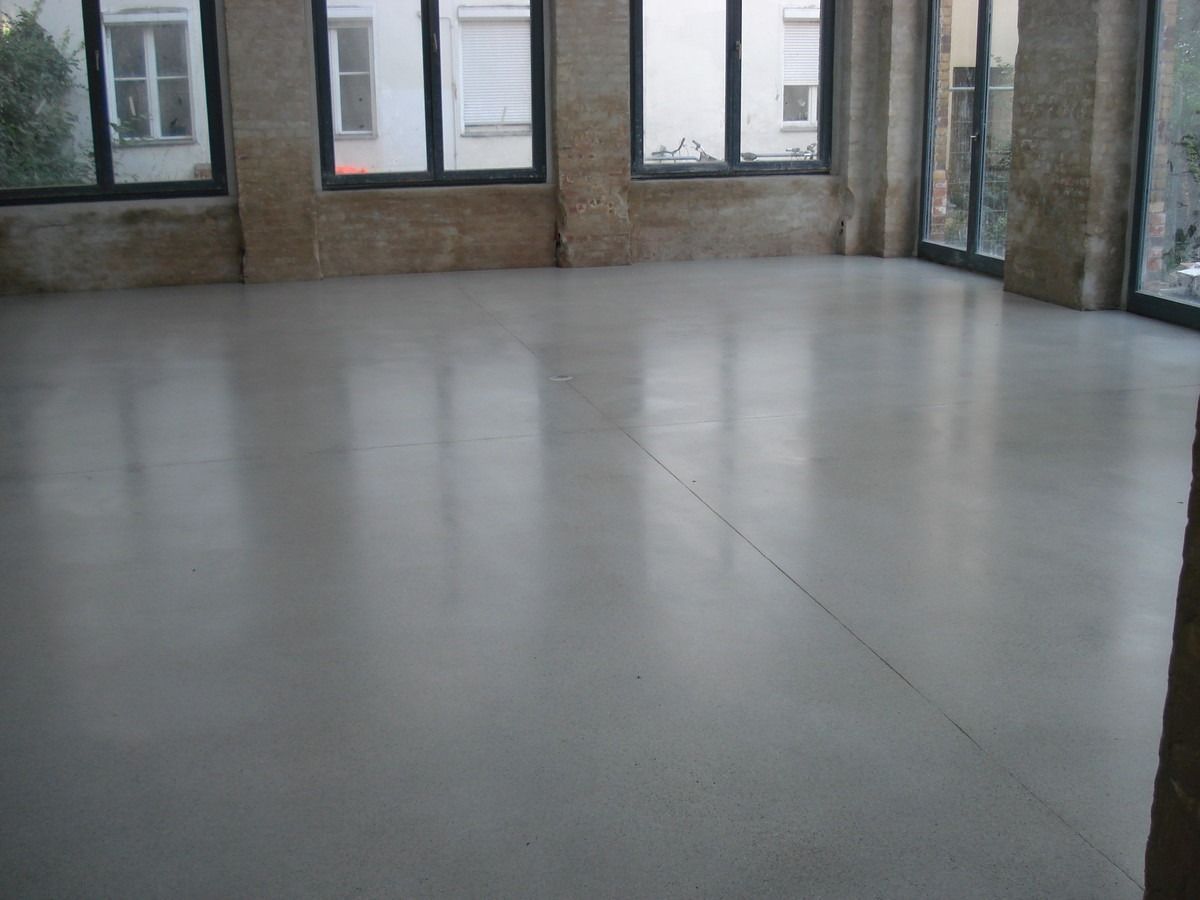 Leerer Raum mit hellgrauem, glänzendem Betonboden und großen Fenstern.