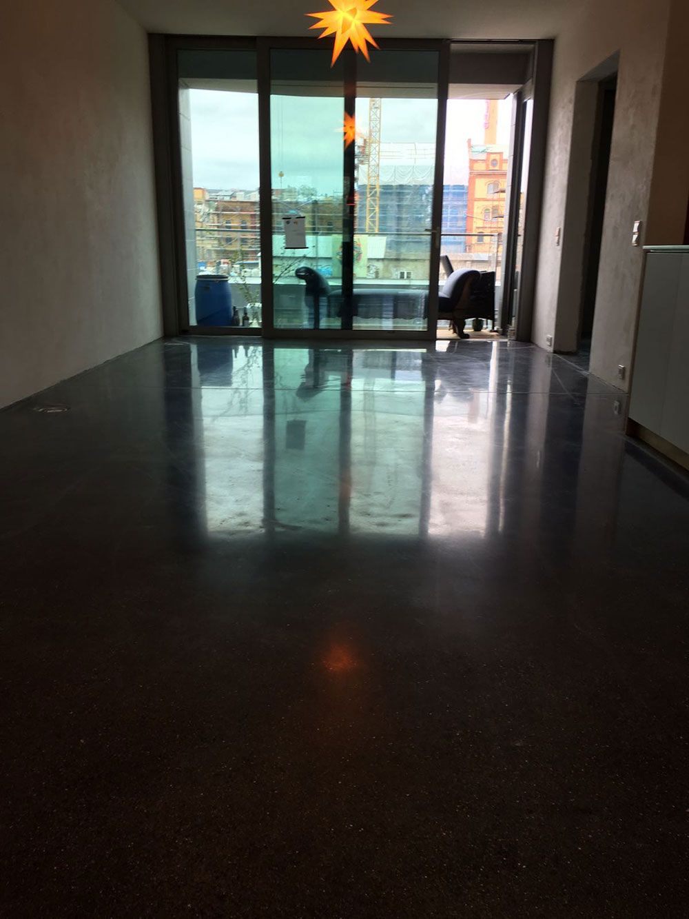 Ein polierter, dunkler Boden reflektiert das Sonnenlicht, das durch eine große Glasschiebetür fällt. Innenansicht.