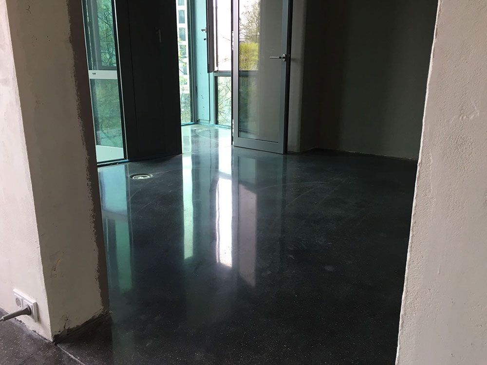 Ein leerer Raum mit einem polierten, spiegelnden dunklen Boden. Fenster lassen helles Licht herein.