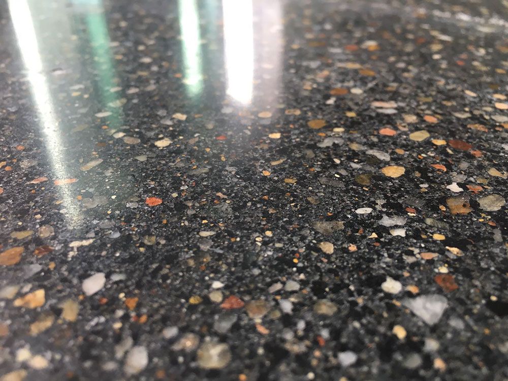 Nahaufnahme einer polierten, dunkelgrauen Betonoberfläche mit freiliegendem Zuschlagstoff in verschiedenen Farben.