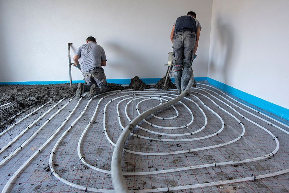 Arbeiter verlegen in einem Raum einen Betonboden über den Heizrohren.