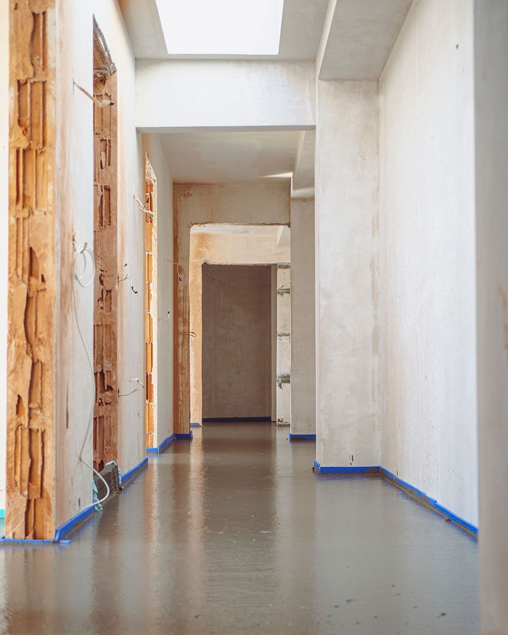Ein Flur im Umbau mit glattem, nassem Boden. Sichtbare Ziegelwände und weiße Wände sind erkennbar.