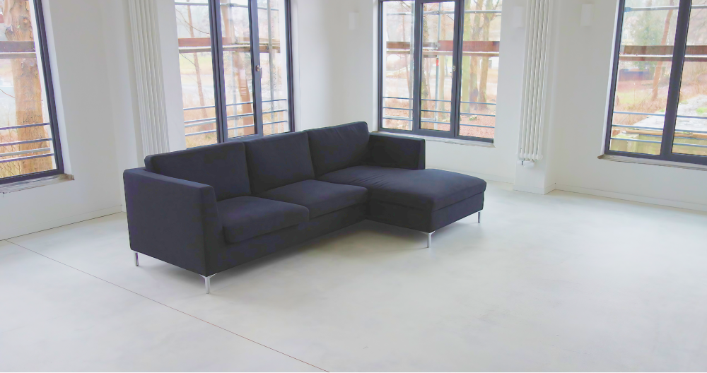 Ein modernes, dunkelblaues Ecksofa in einem hellen, weißen Zimmer mit großen Fenstern.