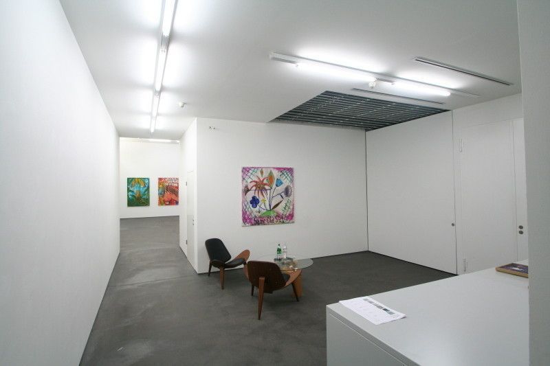 Galerieinterieur mit weißen Wänden, Kunstwerken, zwei Stühlen und einem kleinen Tisch.