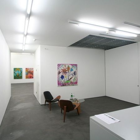 Interieur einer modernen Kunstgalerie mit Gemälden an weißen Wänden, Sitzbereich und Deckenbeleuchtung.