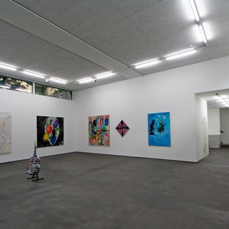 Eine Kunstgalerie mit weißen Wänden und Gemälden, grauem Boden und Neonlicht.