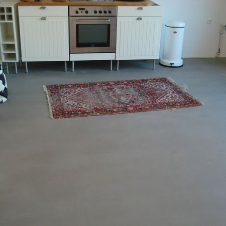 Küche mit weißen Schränken, Backofen und rotem Teppich auf grauem Boden.