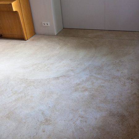 Beigefarbener Raum mit Betonboden. Im Hintergrund eine Holztür und eine weiße Wand.