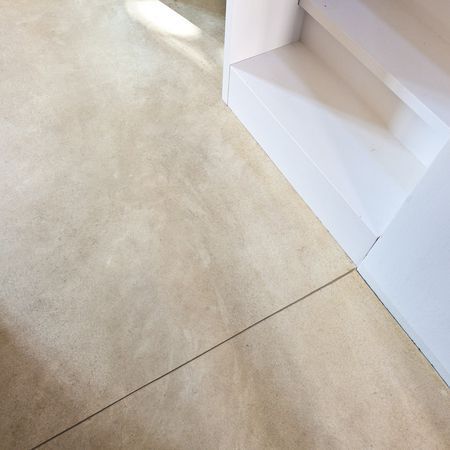 Beigefarbener Betonboden neben einem weißen Einbauregal. Eine dunkle Linie verläuft über den Boden.