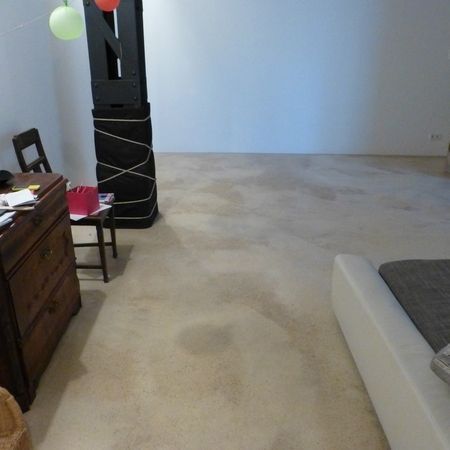 Raum mit hellem Betonboden, weißen Wänden, schwarzer Stützsäule mit gekreuzten Seilen und Möbeln.