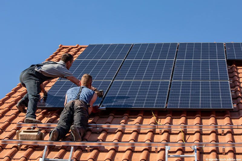 Zwei Männer installieren Solarmodule auf einem Dach.
