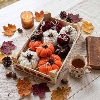 Herbstliche Geschenkbox mit kürbisförmigen Leckereien, Kerzen, Tannenzapfen und Herbstlaub auf einem Tisch