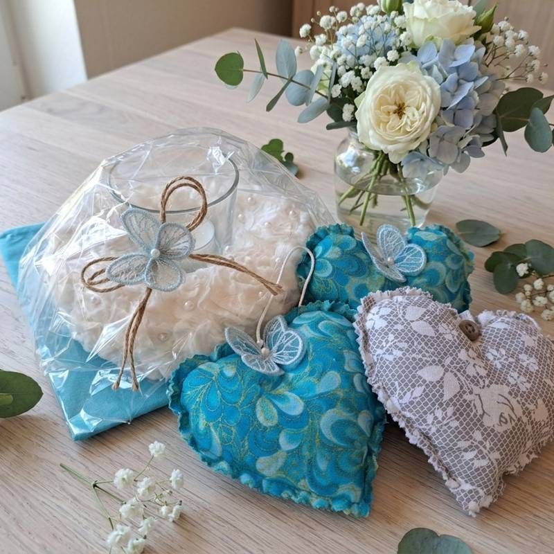 Verschiedene herzförmige Geschenksäckchen aus Stoff in Blau und Spitze auf einem Tisch neben einem Blumenstrauss.