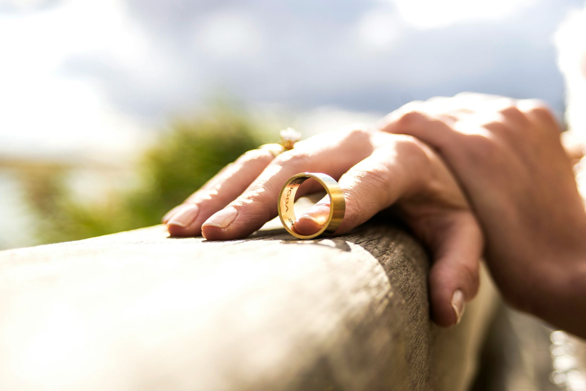 Mano apoyada en la repisa, anillo de bodas visible; fondo de cielo borroso.